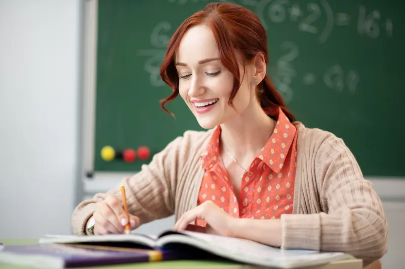 A young teacher sits at her desk and writes in a gratitude journal to avoid teacher burnout. 