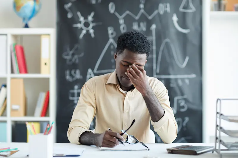 Male teacher holding the bridge of the nose and looking upset because of teacher burnout. 