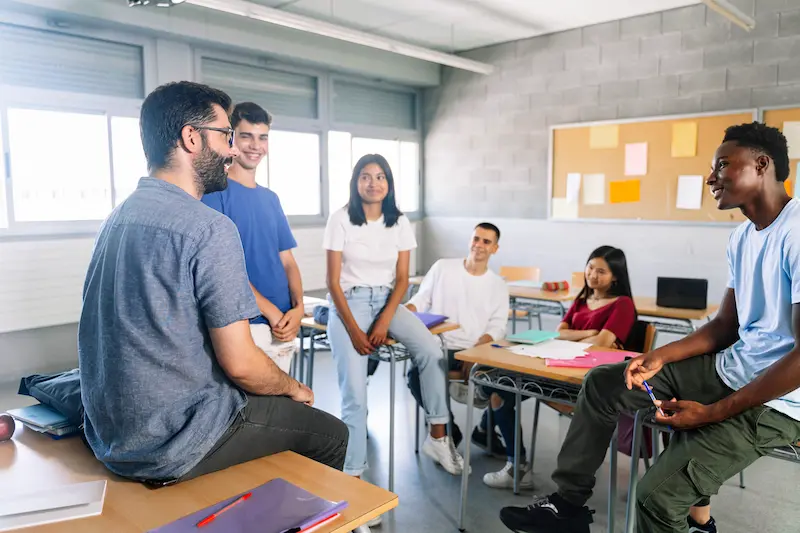 A male teacher leads a class discussion at a high shool.   