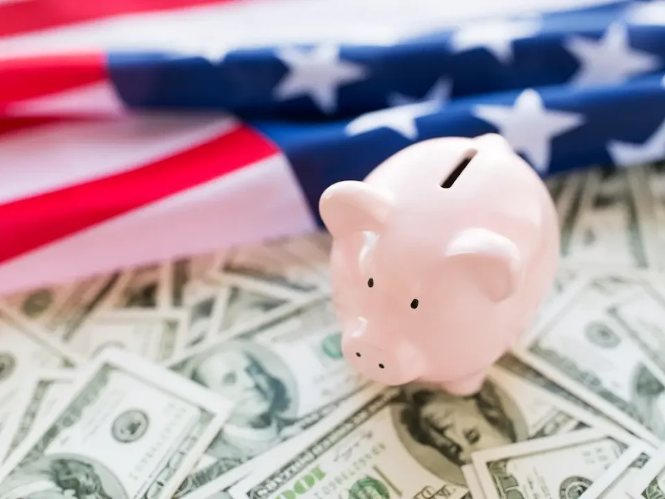 Piggy bank resting on top of money with an American flag in the background