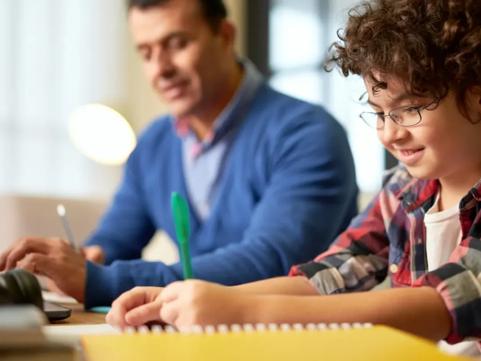 Father and son sit at table while son completes his homework