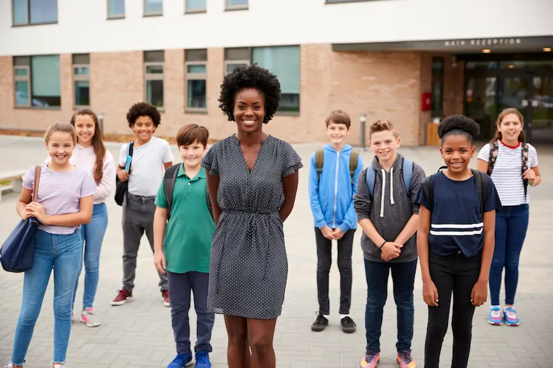 A teacher and her class smile outside of the school.
