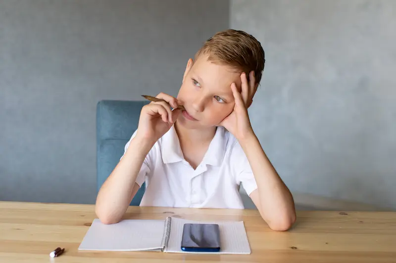 Schoolboy thinking and writing in notebook. 