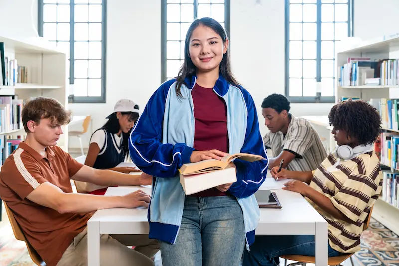  Student smiling and holding a book in a library.  
